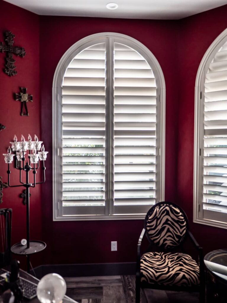 Bold red walls and elegant arched shutters create a dramatic, luxurious space.