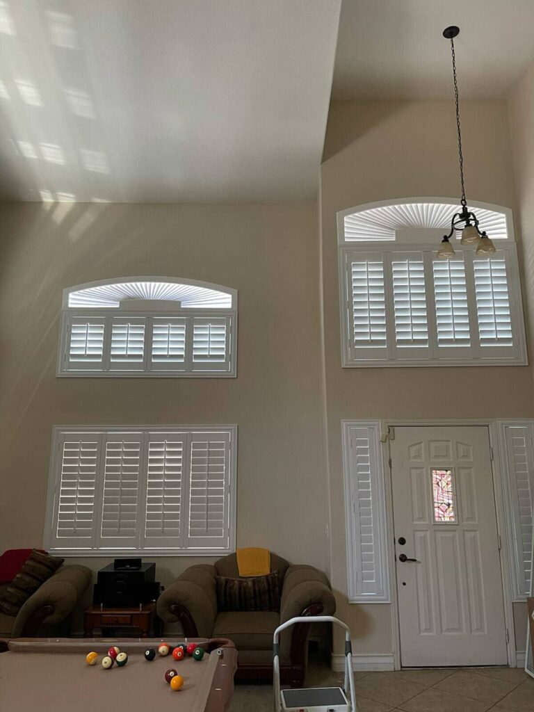 High-ceiling windows with custom white shutters and door panels in the entryway.