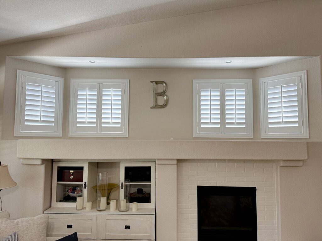 Four small white shutters sit in a custom recessed bay window above a white brick fireplace.