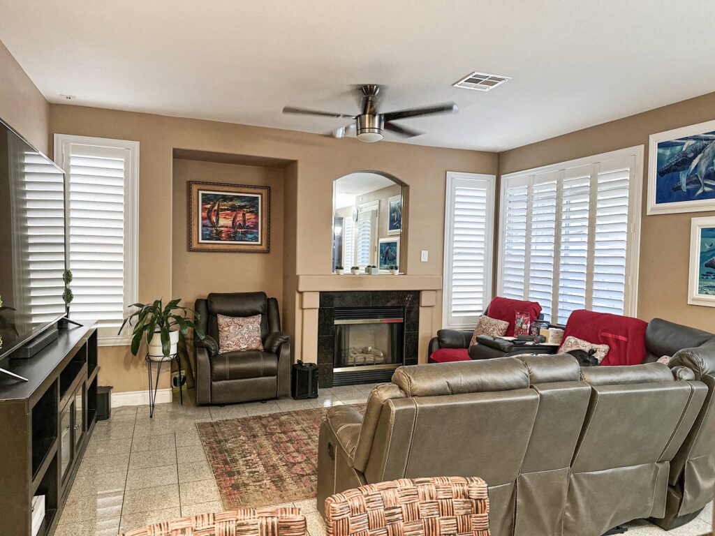 White living room shutters create bright accents around a cozy fireplace and leather seating.