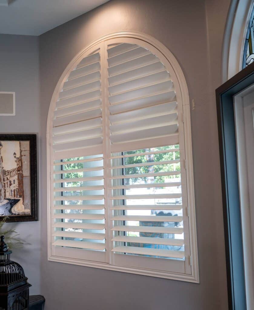 Custom white bedroom shutters are perfectly fitted to this elegant, light-filtering arched window.