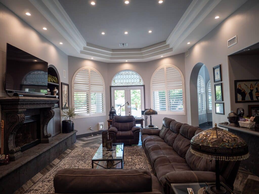 Plantation shutters on arched window illuminated by recessed lights.