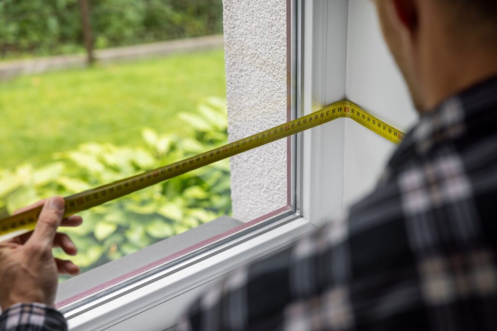 A man measures his windows with a measuring tape.